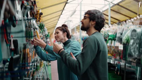 retrato de una pareja joven positiva en la tienda de jardín, eligiendo herramientas para el jardín