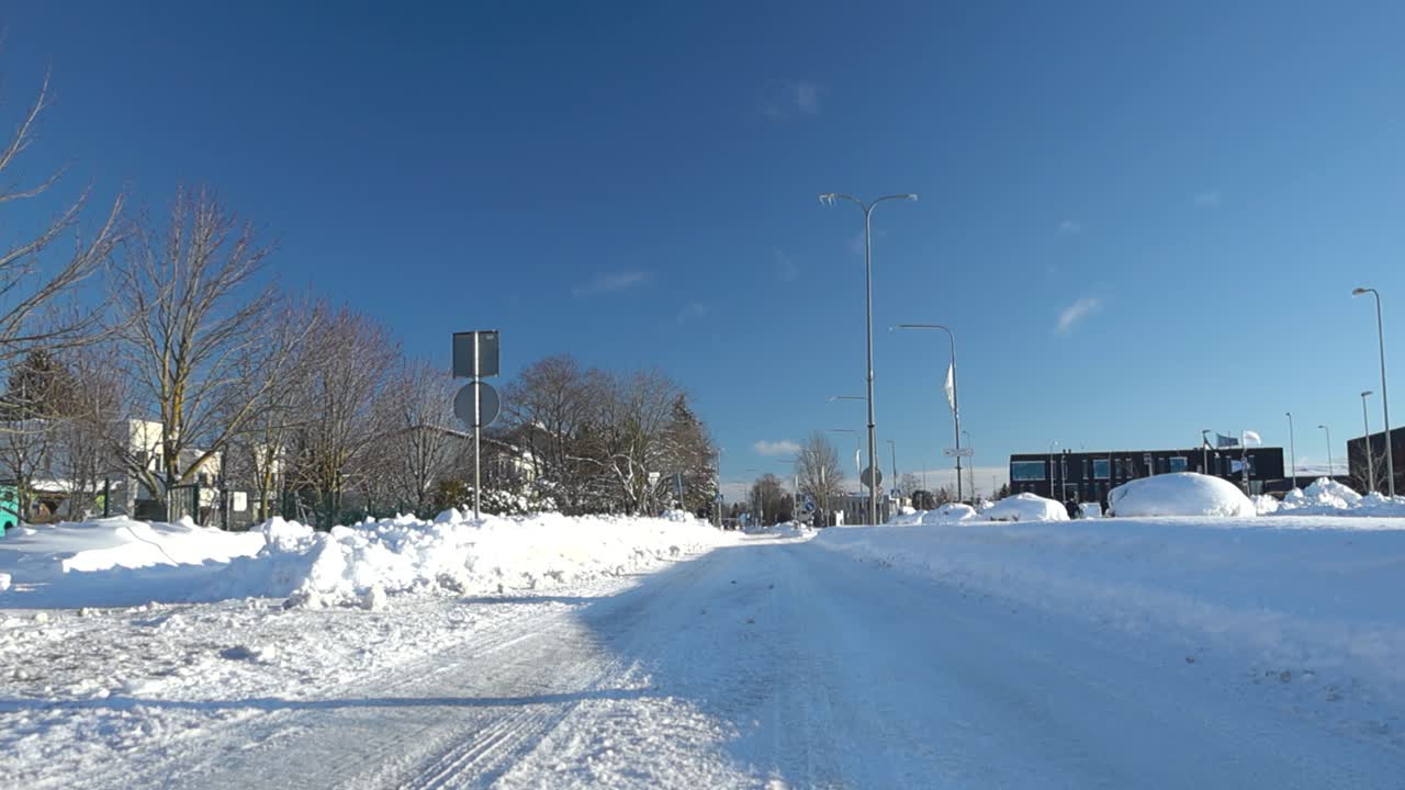 Low angle footage of a winter road for vehicles and cars in Laagri during sunny day. The road is empty with no cars and is covered with thick white fluffy snow that as tire tracks on it. Blue sky.