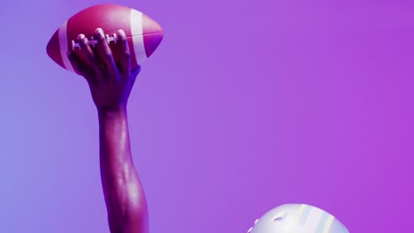 Video-of-african-american-american-football-player-with-ball-over-purple-neon-background