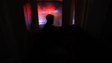 man looking out of window in city onto busy night life