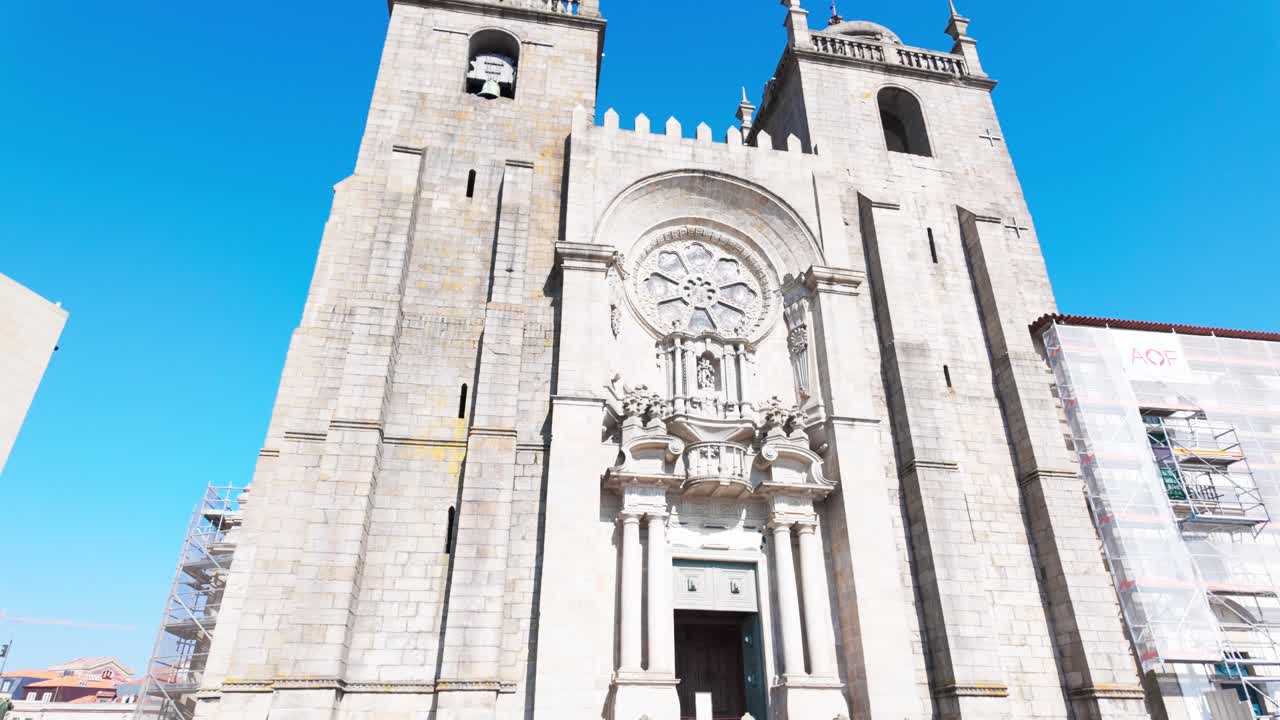 People walking on a sunlit cobblestone plaza near Porto Cathedral, shadow on the ground