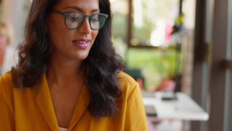 Mature-Businesswoman-Wearing-Glasses-Working-In-Office-Writing-In-Notebook-And-Looking-Out-Of-Window