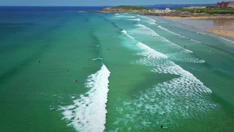 fistral beach surfers riding the newquay waves in cornwall, aerial tracking shot