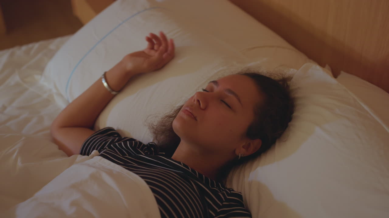 En rolig kvinde hviler fredeligt efter rejsen. En afslappet kvinde sover trygt i et blødt oplyst hotelværelse. En fredfyldt dame nyder en hvilende søvn i et behageligt hotelmiljø efter at have rejst.