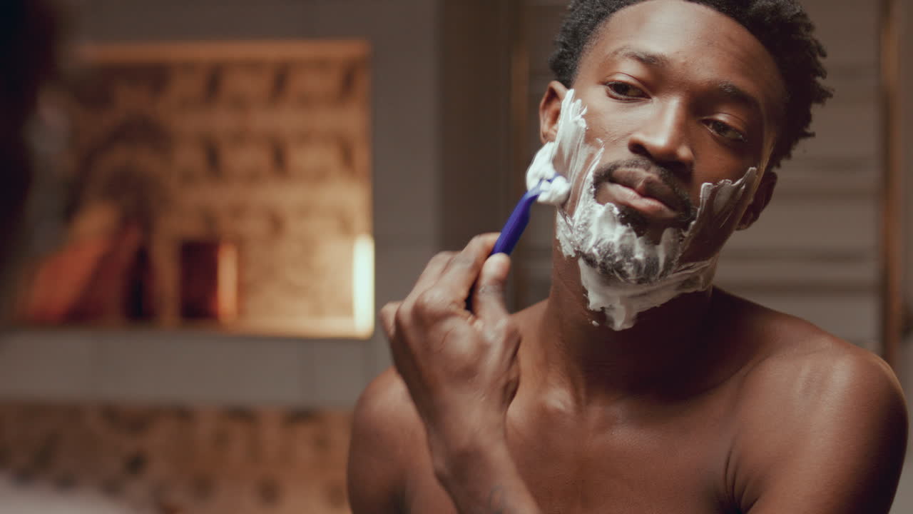 Black Man Shaving His Face in front of Mirror in Bathroom