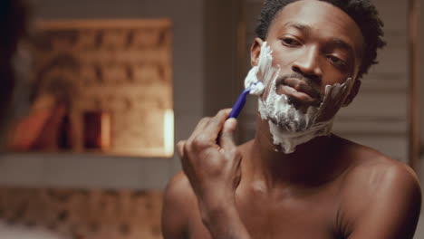 black man shaving his face in front of mirror in bathroom