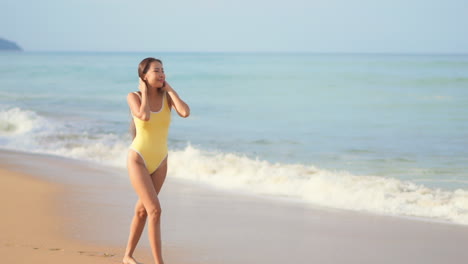 A-pretty-young-woman-in-a-yellow-bathing-suit-walks-along-the-shore-welcoming-the-incoming-waves