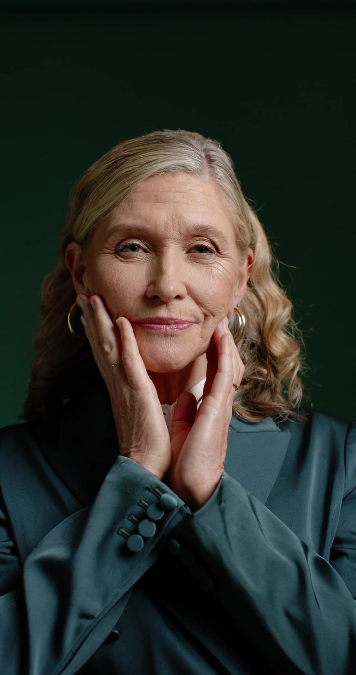 Vertical video: Mature woman posing and cupping face while adjusting hands in studio in teal blazer