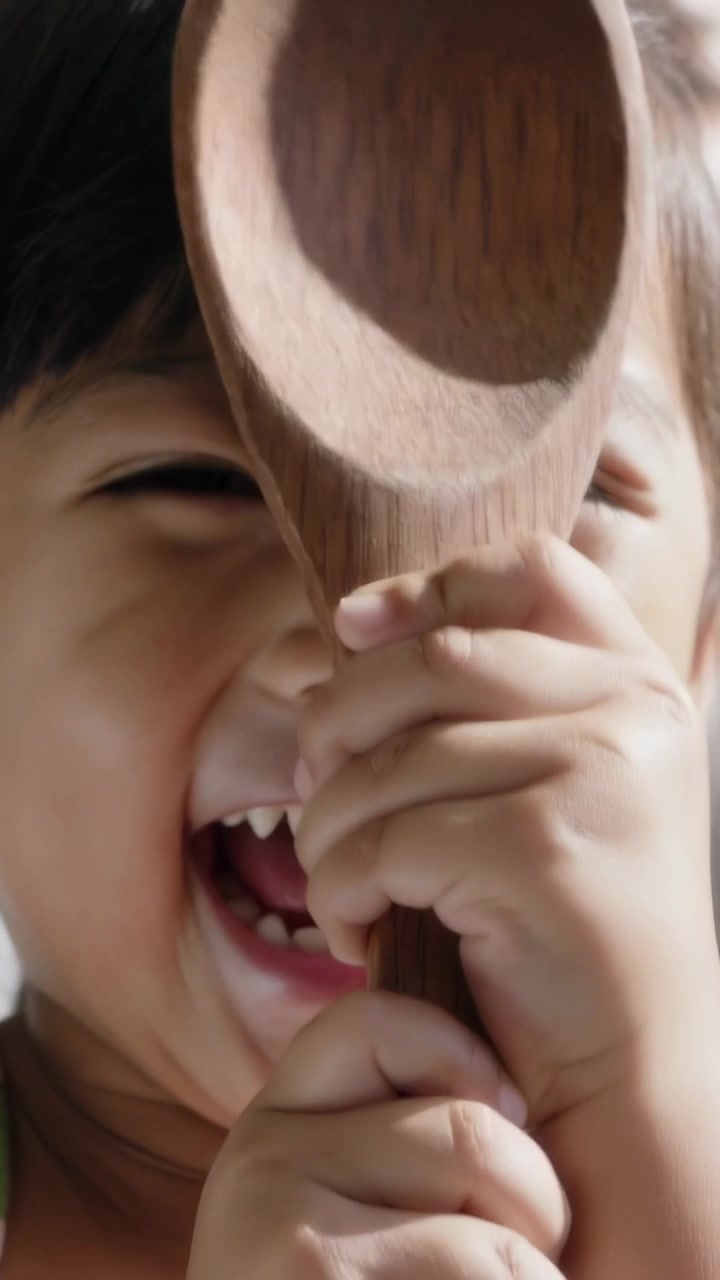Video verticale: Bambino che aggiusta la presa e sbircia in cucina, cucchiaio di legno e cinghie, due mani che giocano