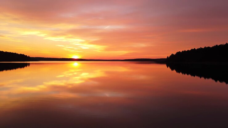 Vibrant sunset reflecting on a calm lake with silhouetted trees
