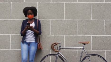 Mujer-Afroamericana-Con-Máscara-Facial-Usando-Un-Teléfono-Inteligente-En-La-Calle