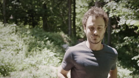 camera tracking a young runner rinning towards the camera in the forest on a hot summer day