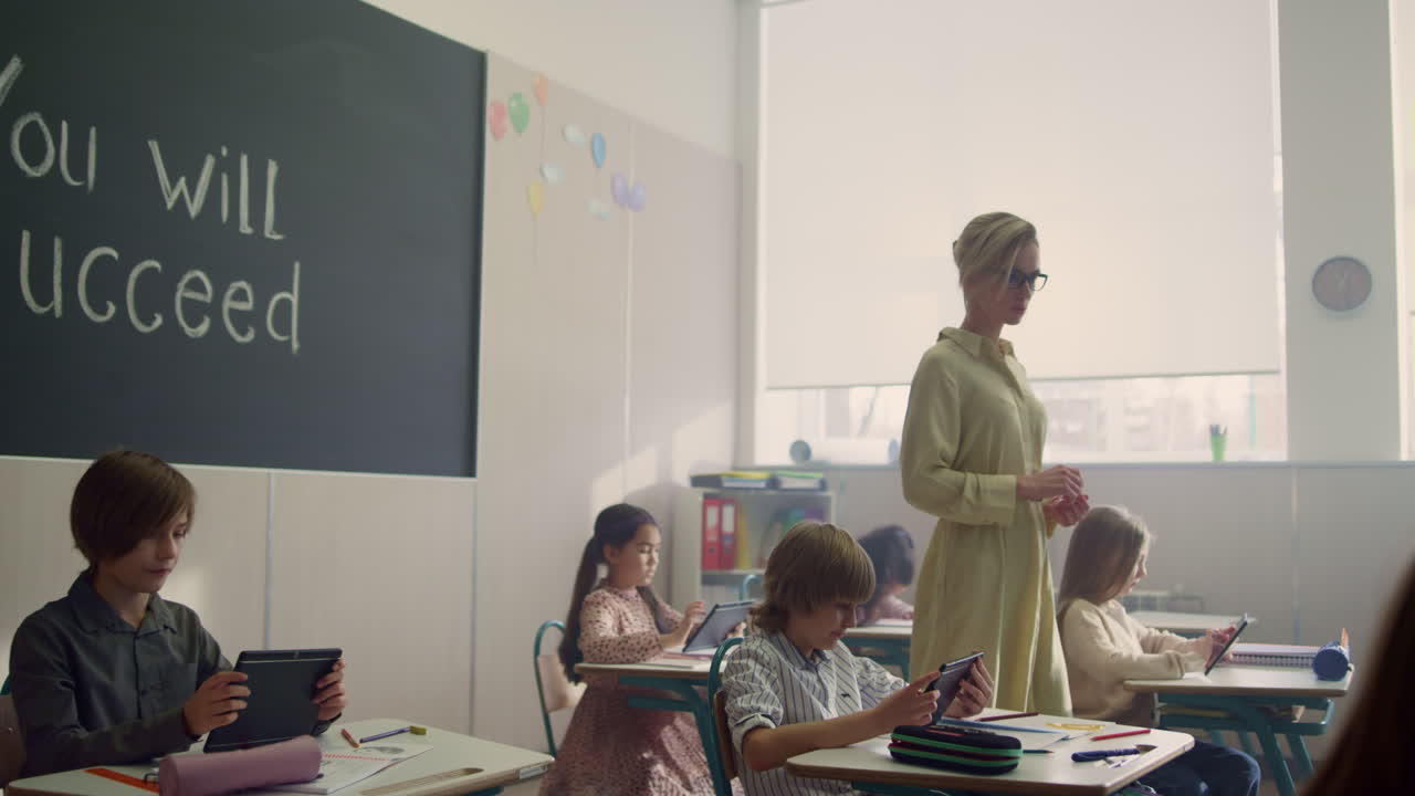 Teacher looking students at lesson. Children learning with digital tablets