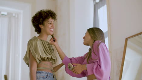mujer caucásica de pelo largo maquillando a su amiga