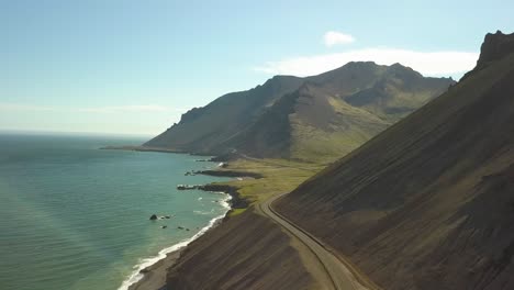 órbita aérea de la carretera de la ladera cerca del mar turquesa, colinas al fondo en la pequeña ciudad de djúpivogur cerca de los fiordos de islandia durante el día
