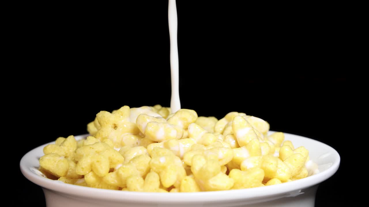 Milk is poured over star-shaped cereal in a white bowl against a black background, creating a dynamic breakfast scene