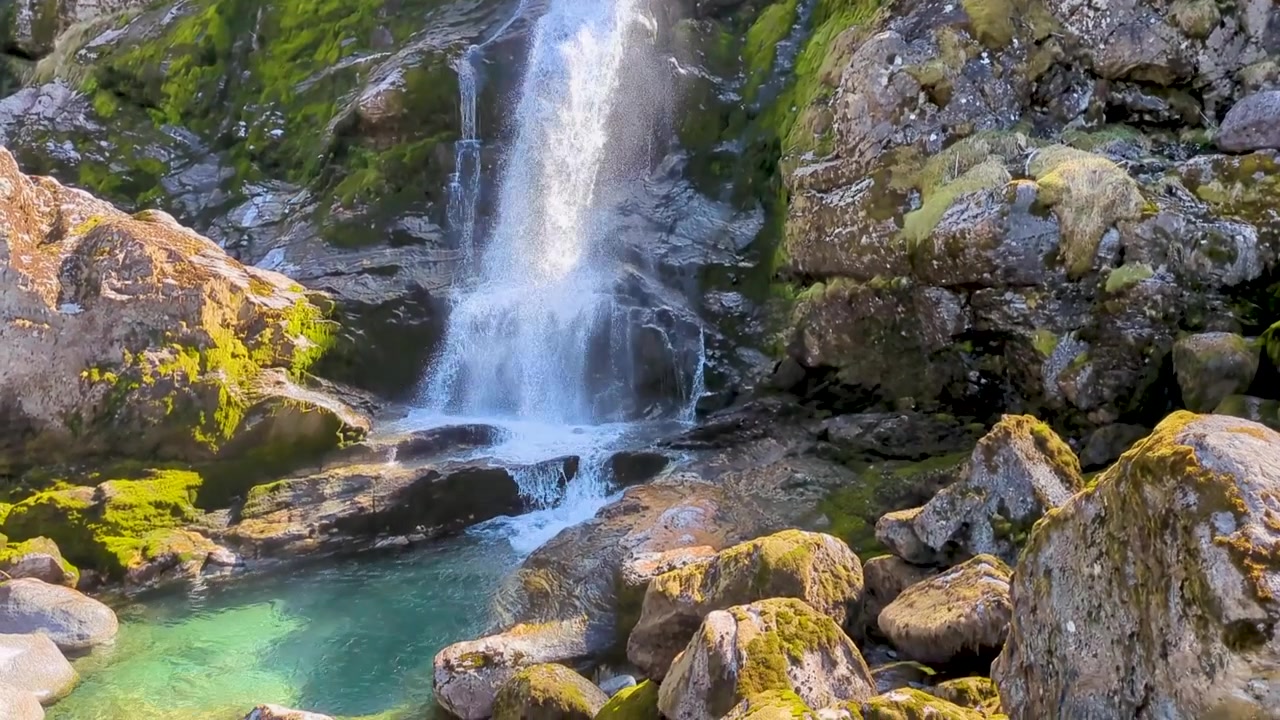 Potente cascata impetuosa che scende da una scogliera rocciosa coperta di muschio al Ghiacciaio di Briksdal, Norvegia - Giorno di sole.