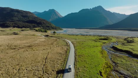 scenic aerial view of campervan traveling through green plateau of rugged mountainous landscape exploring isengard location from lord of the rings in glenorchy, south island of new zealand aotearoa