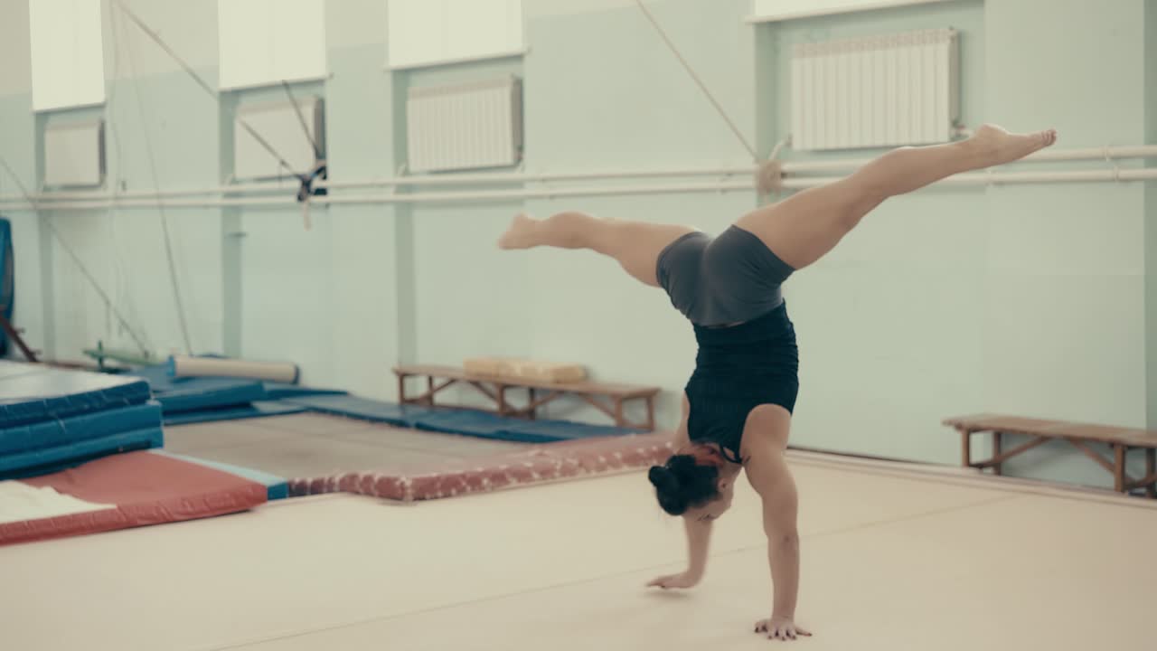 chica atlética en el gimnasio se para en sus manos extiende las piernas a los lados y comienza a girar