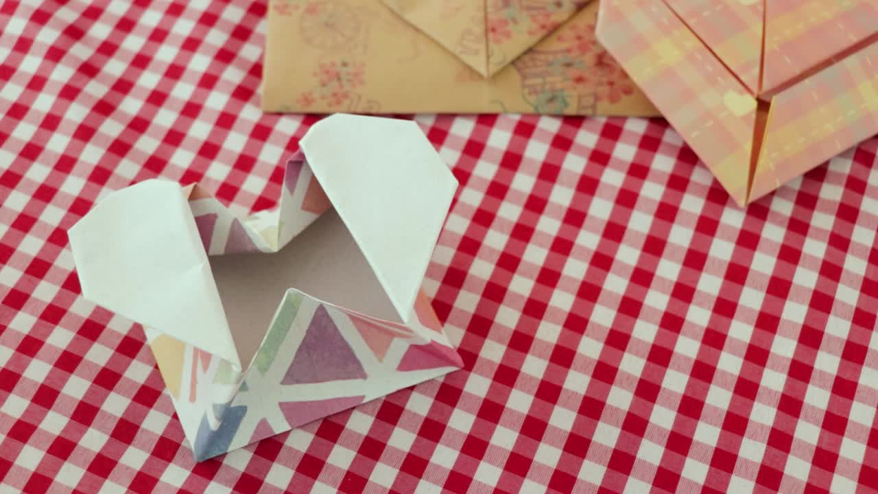Folded heart-shaped origami paper envelopes on checkered tablecloth