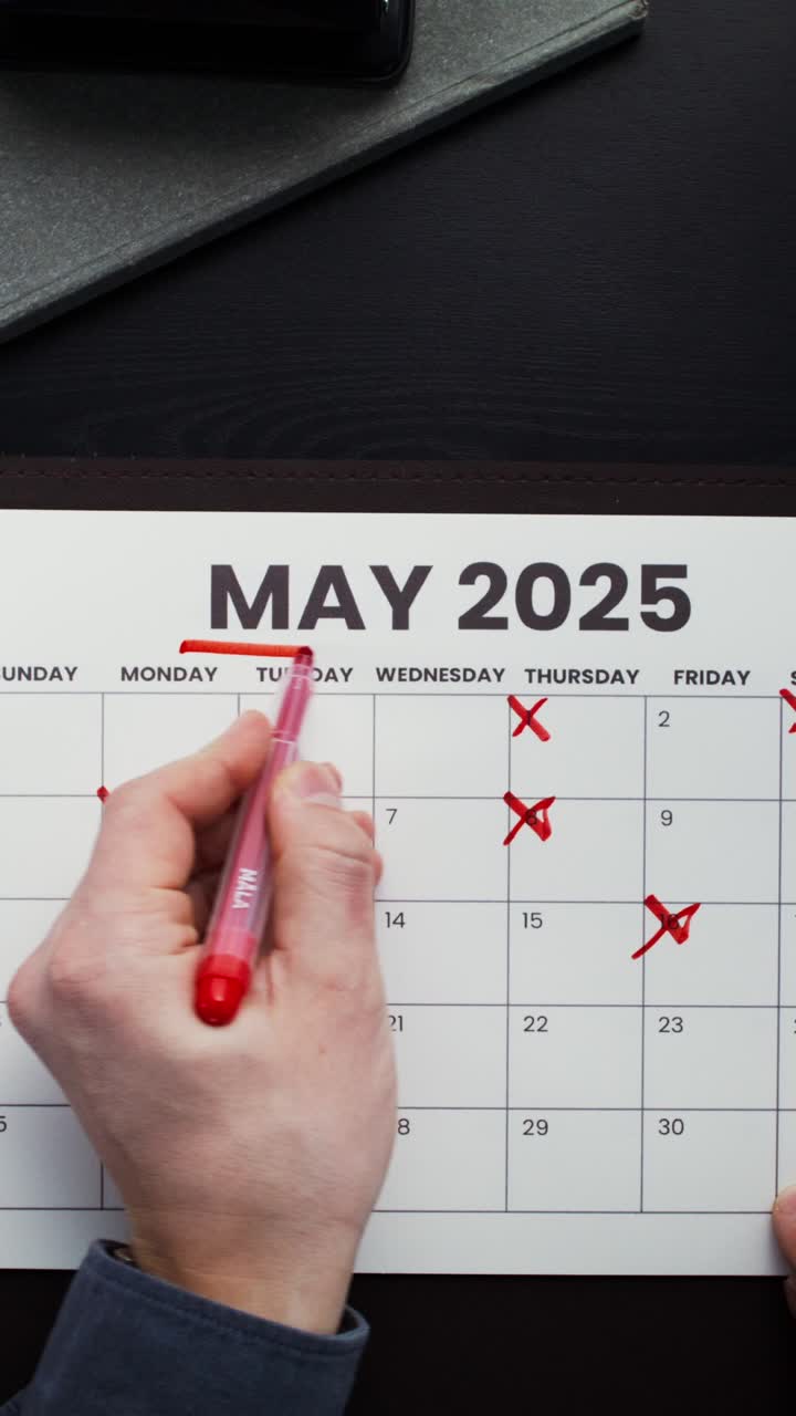 Person crossing out dates on a May 2025 calendar