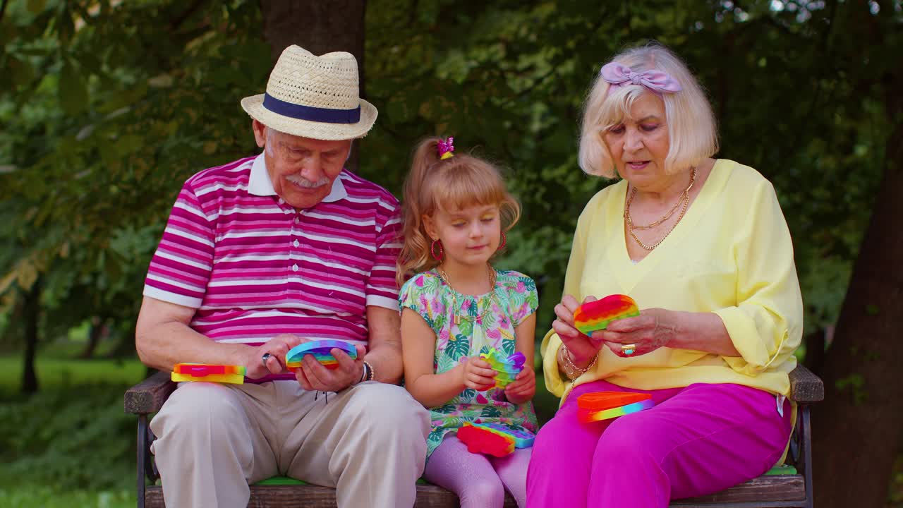 Lächelnde Großeltern und Enkelin spielen mit einem Anti-Stress-Spielzeug.