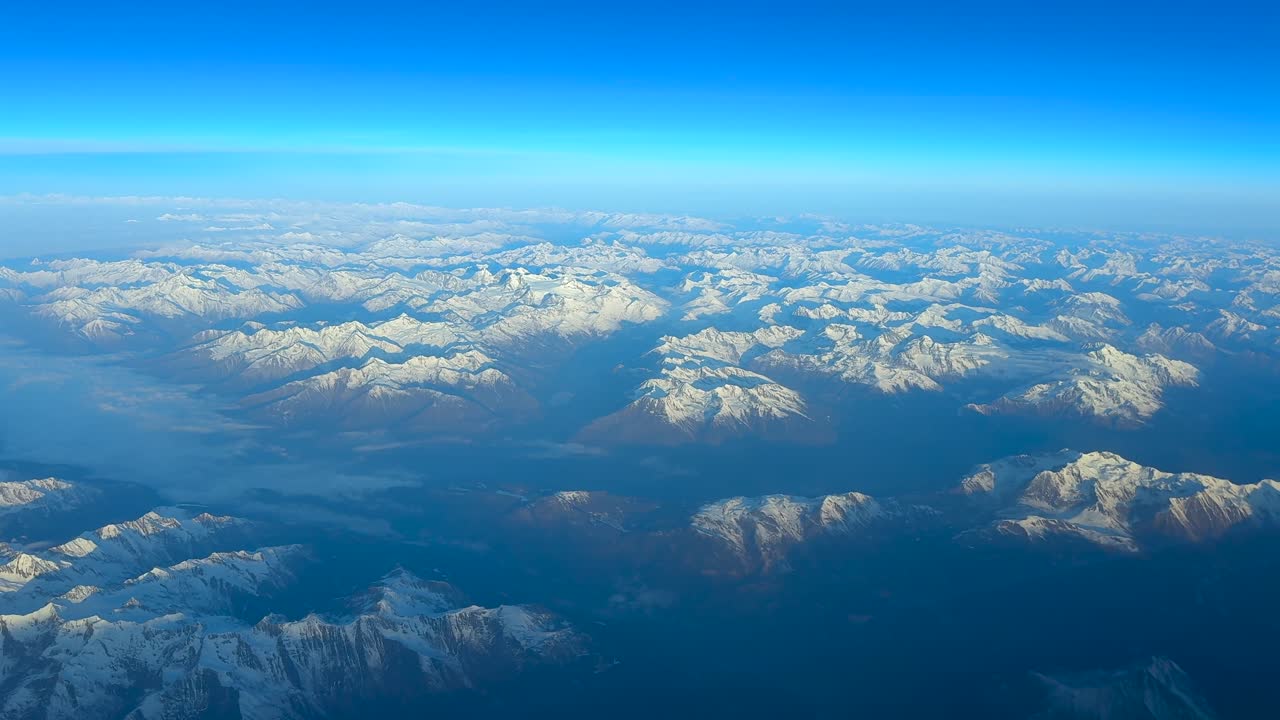 朝日を浴びて飛行する飛行機のコックピットから見た、アルプス山脈の高度な空撮。柔らかな太陽光が景色を包み込んでいます。