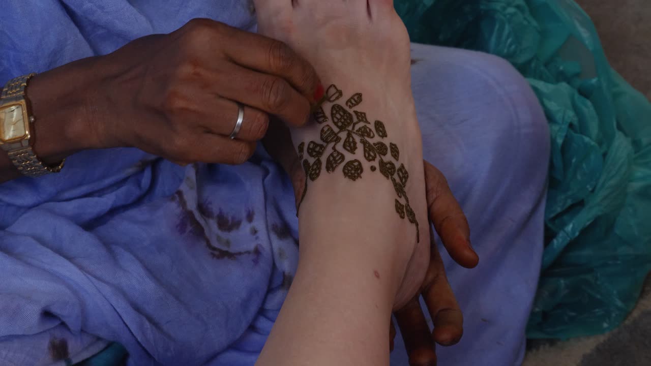 Un'inquadratura delle mani di una donna di colore che dipinge il piede di una donna bianca con l'henné.