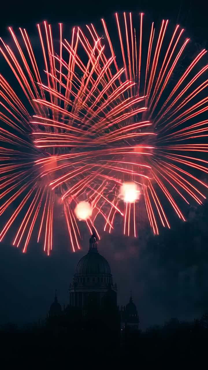 Vertical video: Bursting fireworks sending red sparks fanning above dome silhouette in night sky