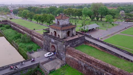 This-footage-captures-the-entrance-to-Hue-Imperial-City-in-Vietnam,-where-modern-vehicles-drive-towards-the-historic-gate