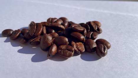 macro shot of many roasted coffee beans lighting during sunlight outdoors on white surface