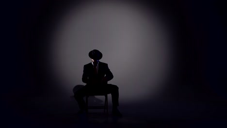 man in hat and suit silhouetted by spotlight on dark stage