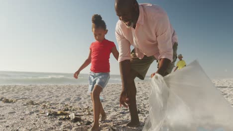 Älteres-Afroamerikanisches-Paar-Mit-Enkelkindern,-Das-Am-Sonnigen-Strand-Müll-Trennt