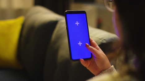 close up over the shoulder shot of woman spending evening at home sitting on sofa looking at blue screen mobile phone 3