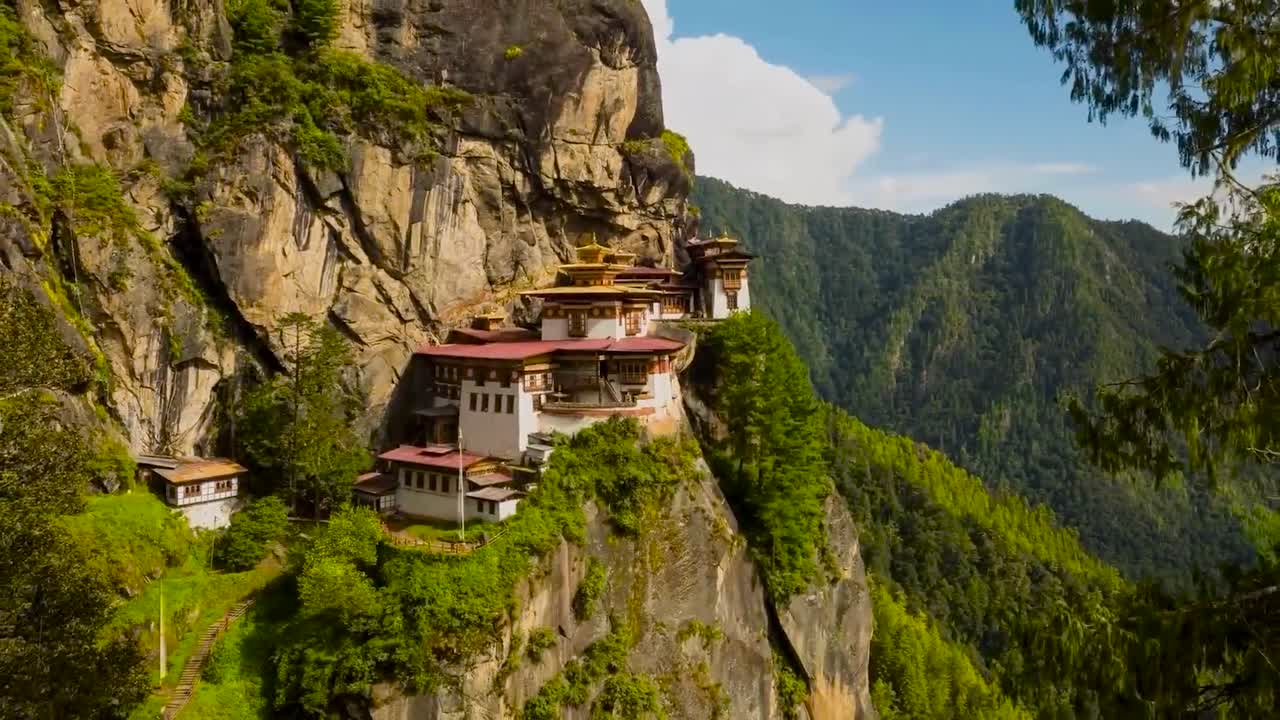 Paro Taktsang or Palphug Monastery old building on a cliff timelapse during a sunny day with cloud shadows moving on the architecture and nature surrounding it. Monastery is white and has red roofing