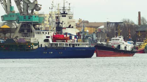 large blue cargo ship leaving port of liepaja , overcast spring day, medium shot from a distance