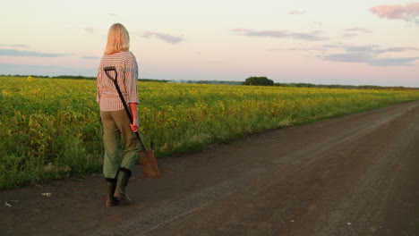 woman walking through a field with a shovel