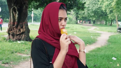 Beautiful-young-afghan-woman-in-hijab-standing-on-lake-and-eats-orange-flavor-ice-cream