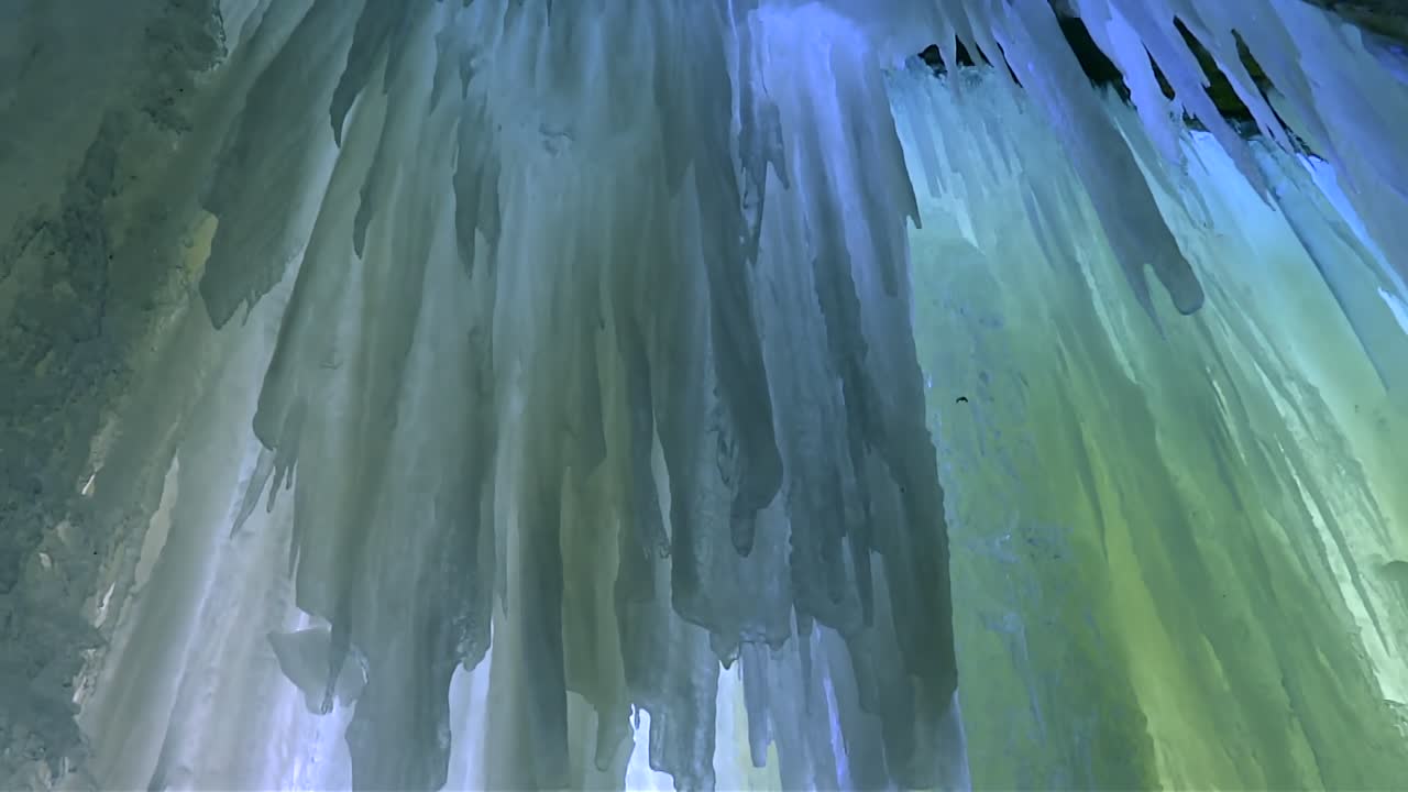 Streaked yellow and blue ice sheets with jagged icicles hang from cave ceiling in close up view, Eben Ice Caves, USA