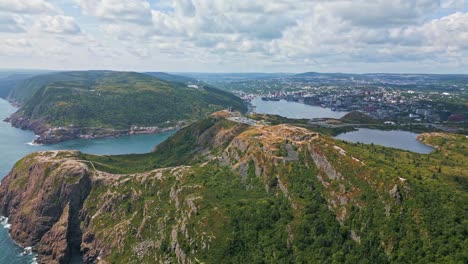 an aerial shot captures the undulating ridges and deep gullies of signal hill, with green slopes descending to a broad valley and distant harbour under a cloud-streaked sky
