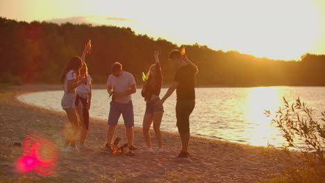 the students celebrate end of educational year on the open air party on the lake coast with beer. it is crazy and hot beach party between the best friends around bonfire.