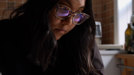 Asian-woman-writes-in-a-notebook-in-her-home-whilst-working-on-her-laptop-computer