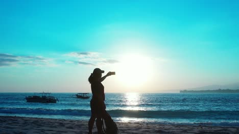 silhouette of girl taking photos on beautiful glowing sunset sky reflecting on sea washing exotic beach in thailand