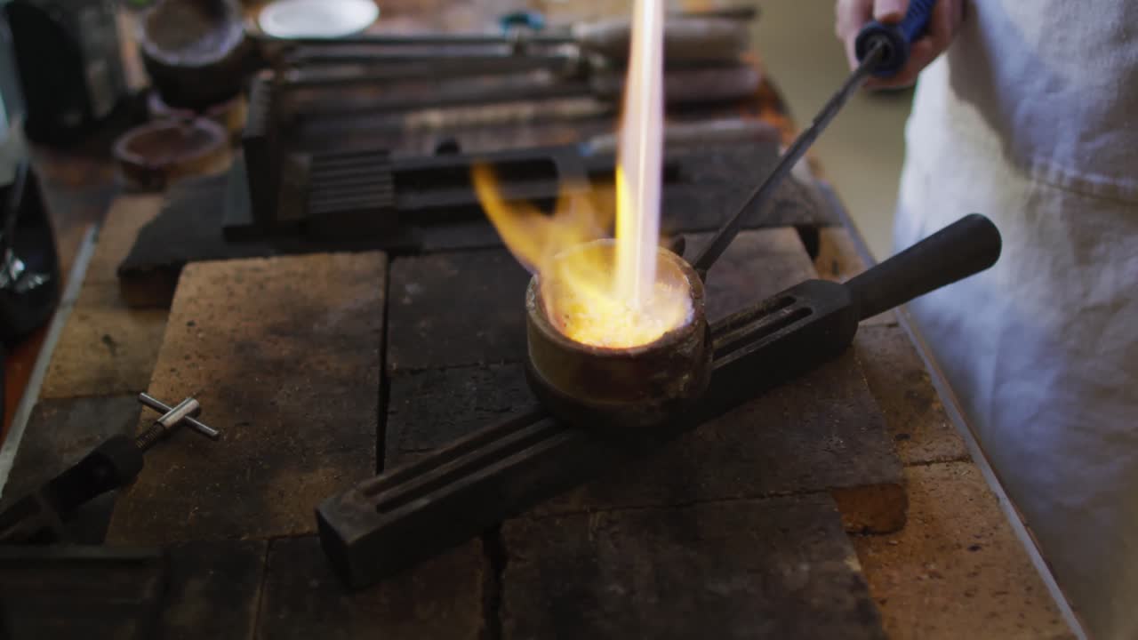 joyería caucásica en el taller con delantal, usando quemador de gas, fundiendo metal
