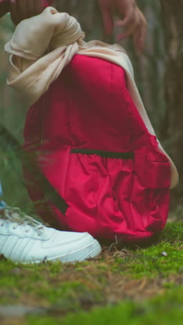 primer plano de mujeres con vaqueros y zapatillas deportivas cerrando las mochilas recuperadas del suelo del bosque, preparándose para la caminata, el terreno de musgo y los árboles altos crean un entorno pacífico y natural