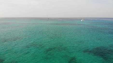 dolly aéreo sobre las hermosas aguas del océano azul turquesa hacia dos catamaranes que navegan en sal cabo verde