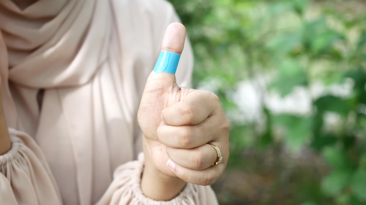 mujer con vendaje en el pulgar dando pulgares hacia arriba