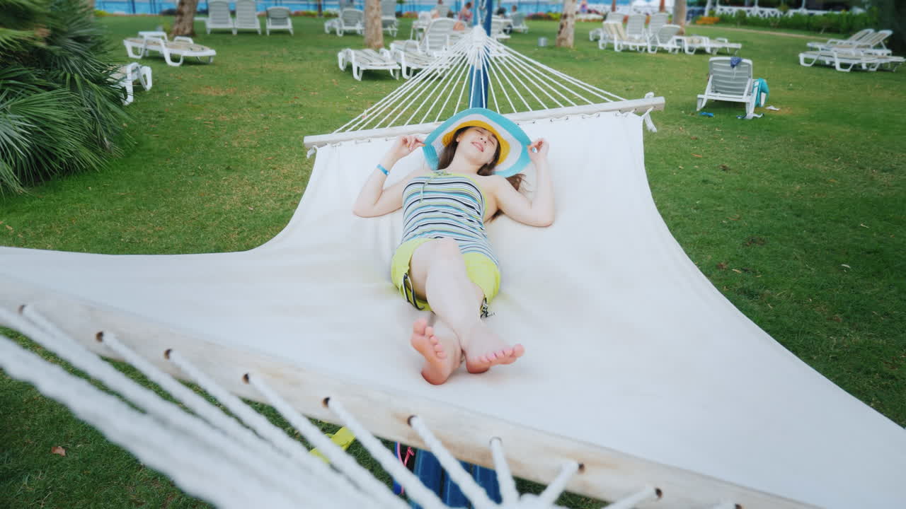 una chica brillante con ropa de colores fríos y un sombrero de ala ancha descansa en la costa del mar en un blanco