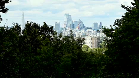 time-lapse viewpoint of the city of london through the trees of one tree hill with skyscrapers in the distance