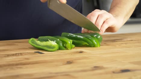 slicing green peppers on a wooden table top with a chef's knife